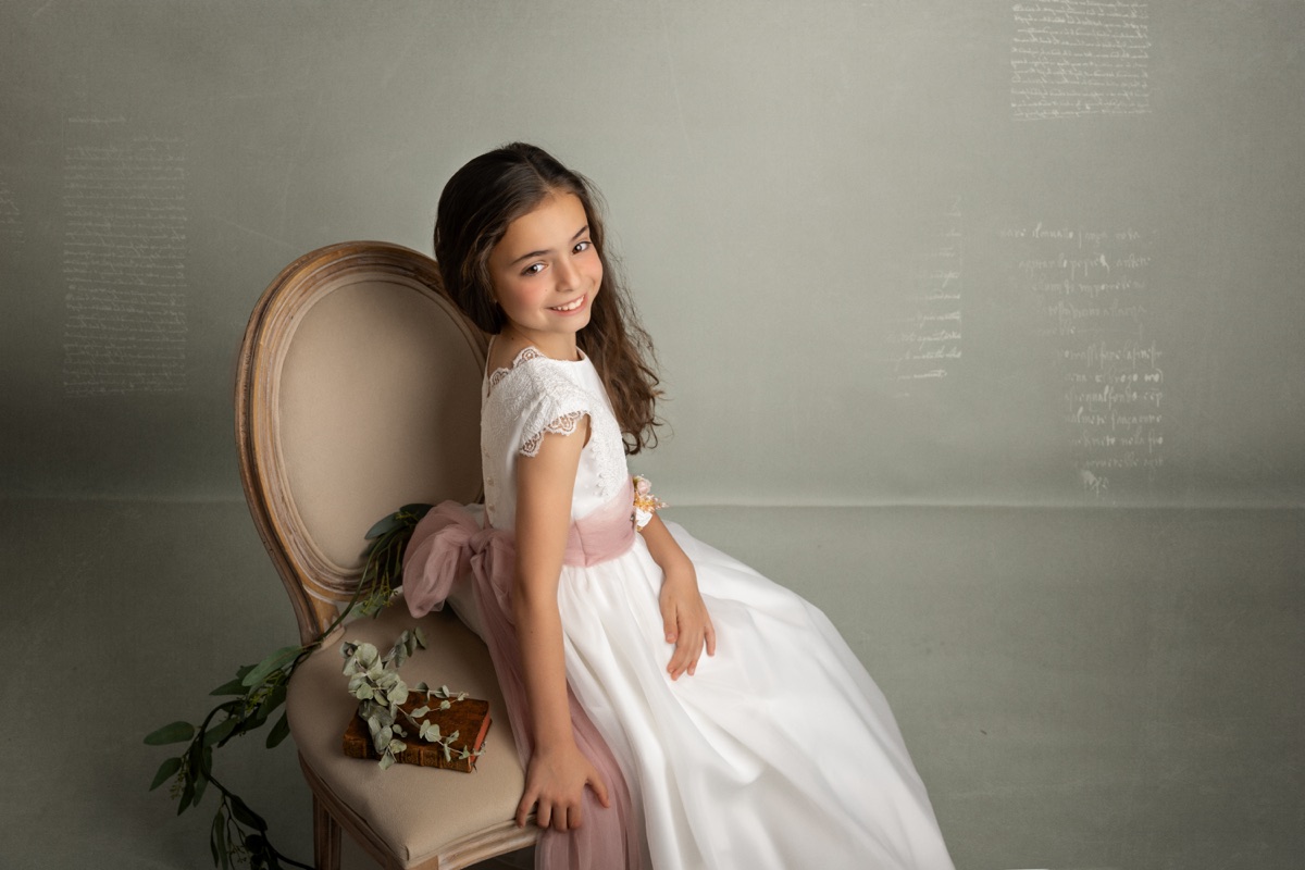 Retrato de una niña de Comunión sentada en una silla de estudio.