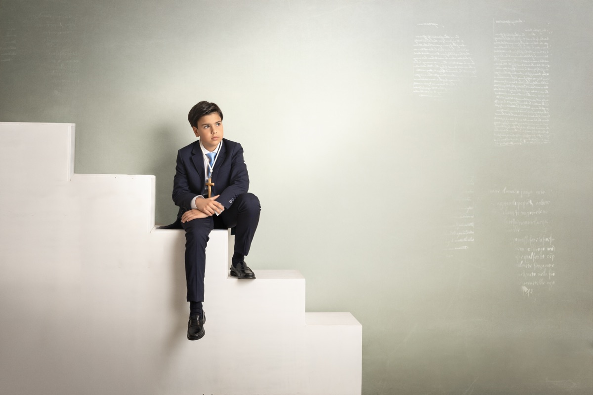 Niño de Comunión sentado en unas escaleras geométricas del estudio.