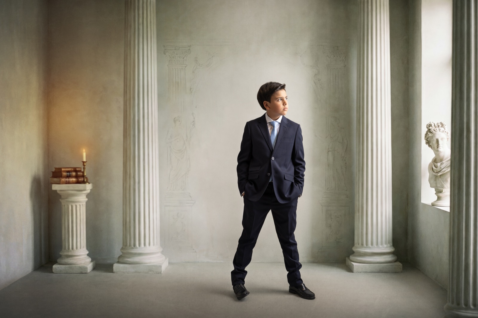Retrato Fine Art de un niño de Comunión con traje oscuro en un escenario de columnas clásicas