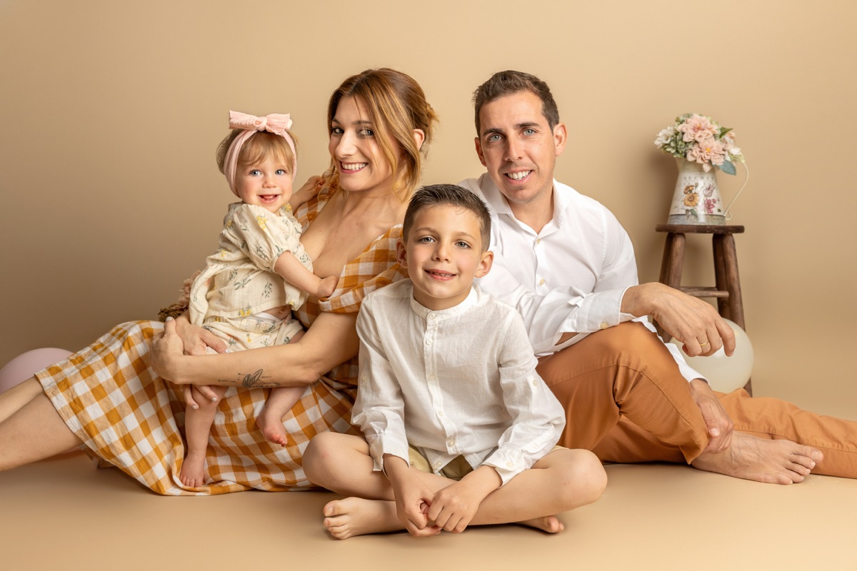 Madre, padre y sus dos hijos posan juntos sobre un fondo cálido