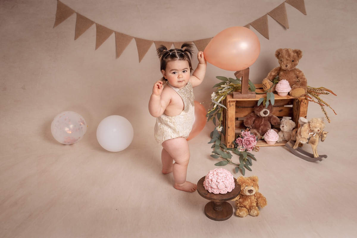 Bebé de pie junto a un globo en un escenario de primer cumpleaños
