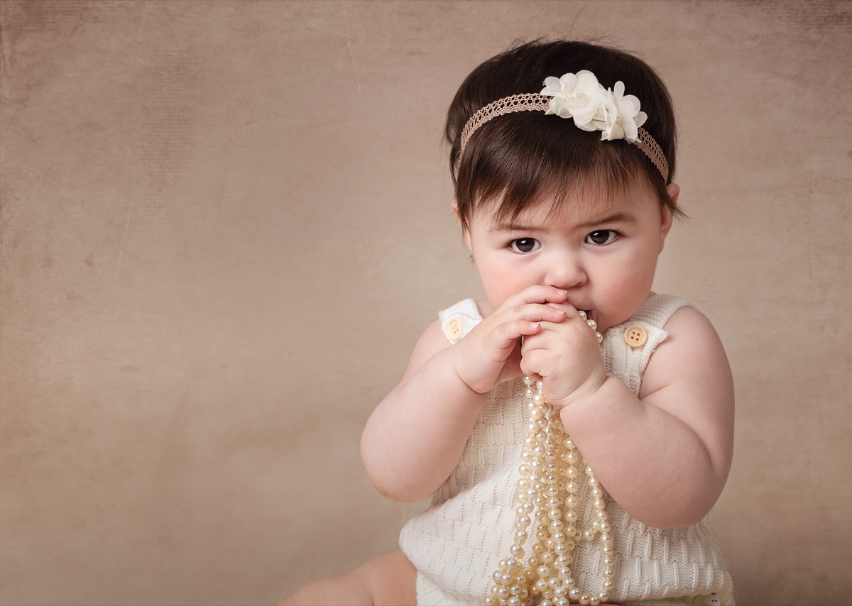 Bebé con una diadema de flores y un collar de perlas entre las manos