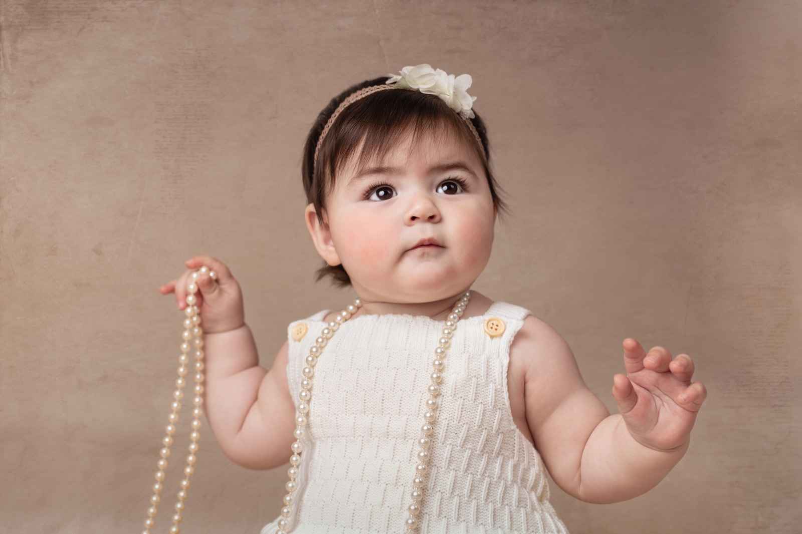 Bebé con un collar de perlas entre las manos durante su sesión infantil