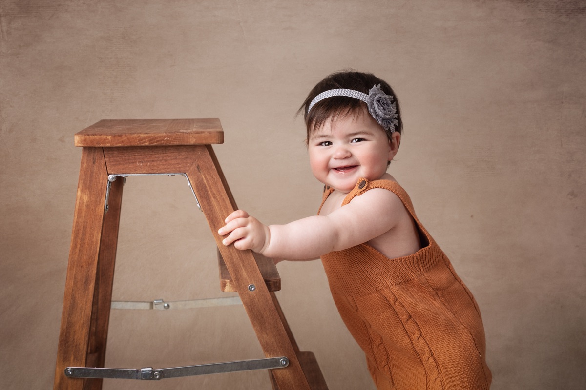 Bebé sonriente junto a un taburete durante una sesión infantil