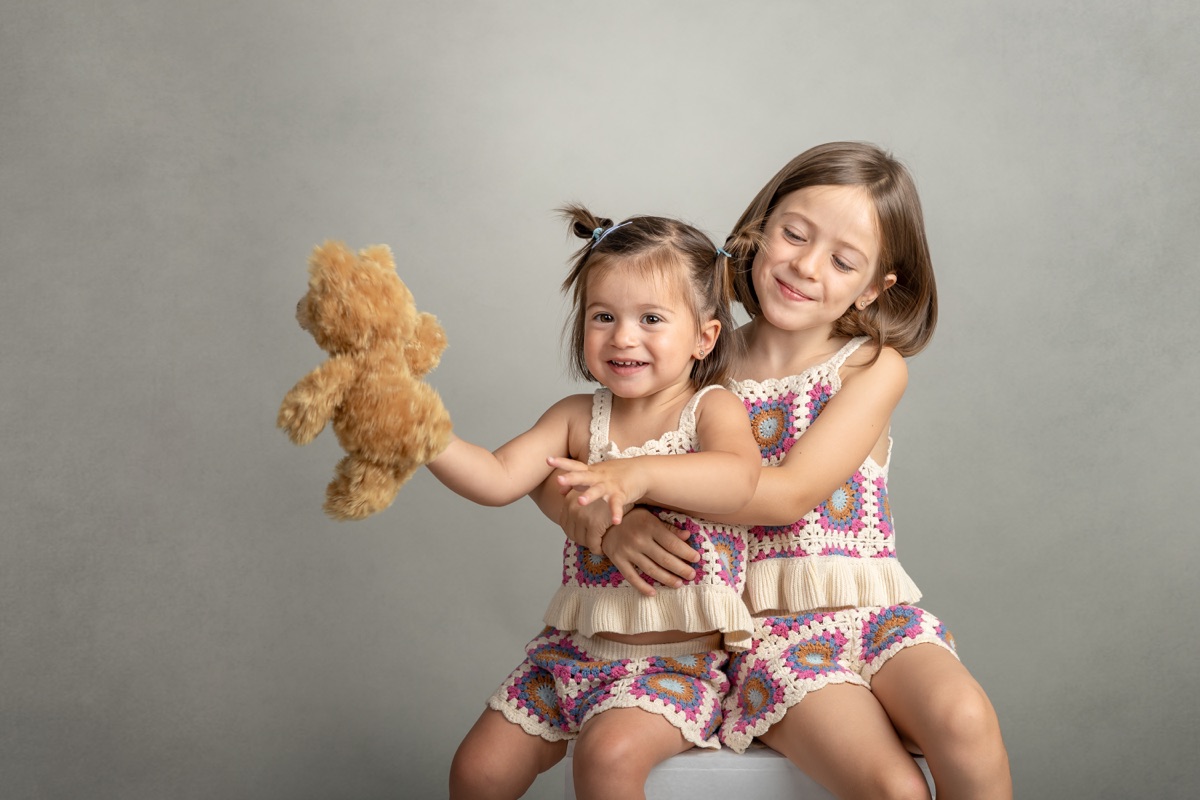 Dos hermanas abrazadas mientras juegan con un peluche durante una sesión infantil