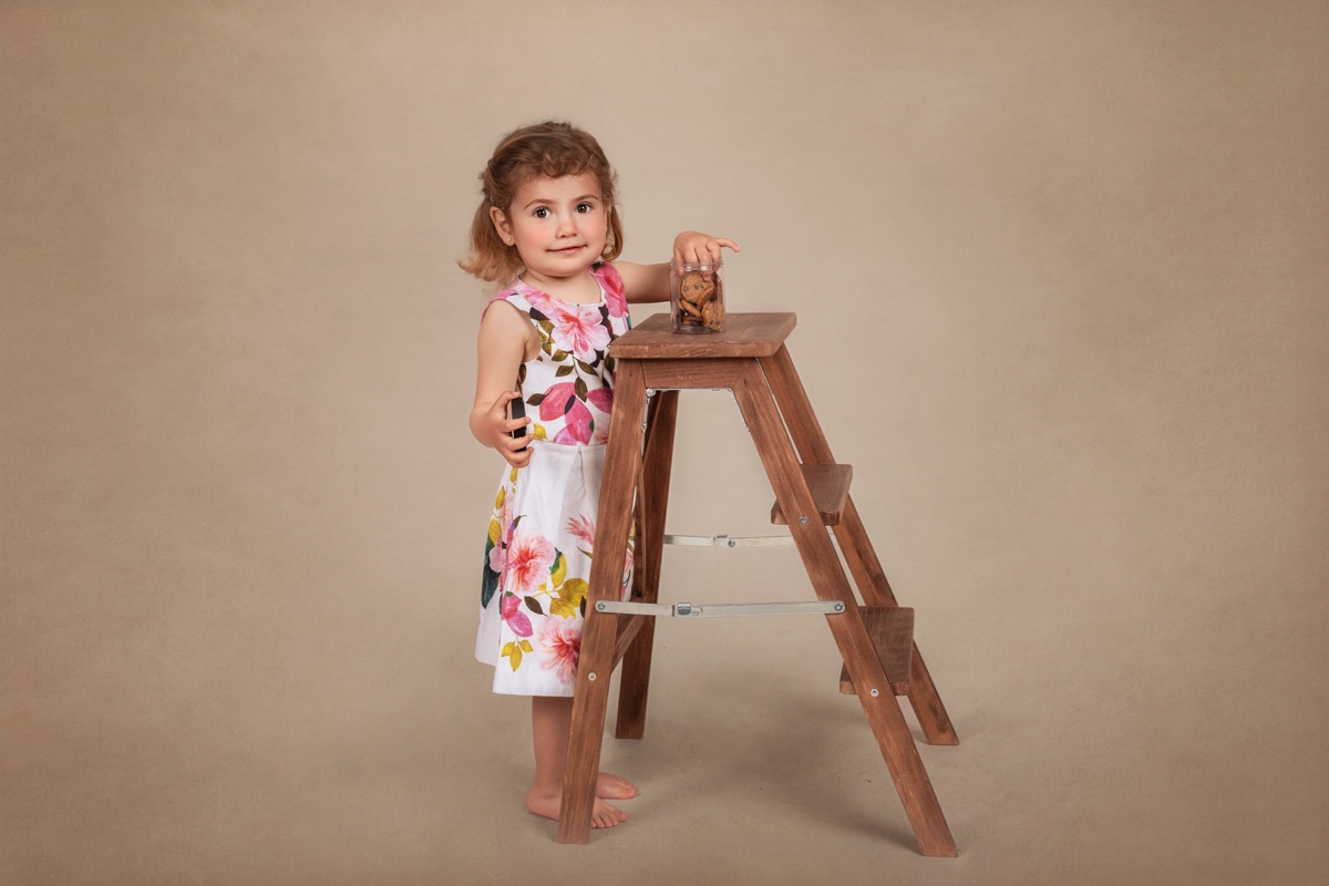 Niña de pie junto a una escalera de madera durante una sesión infantil