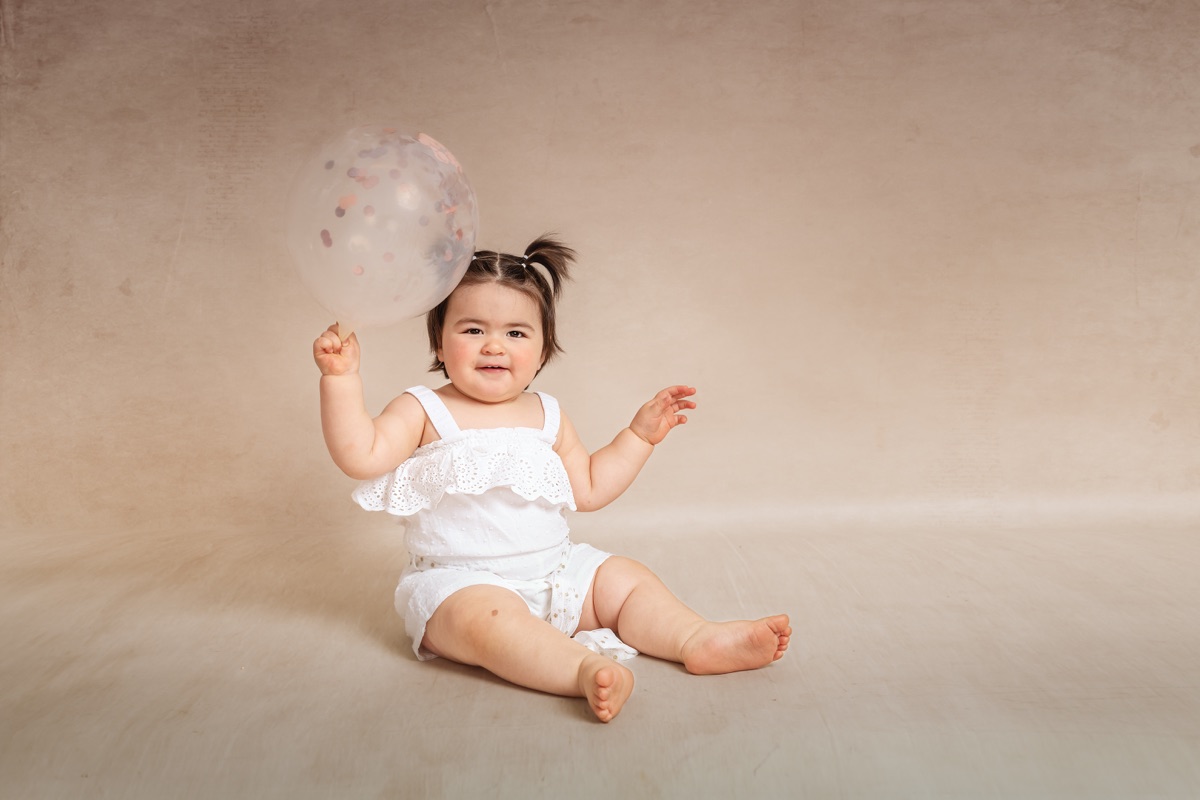 Niña sentada jugando con un globo durante su sesión infantil