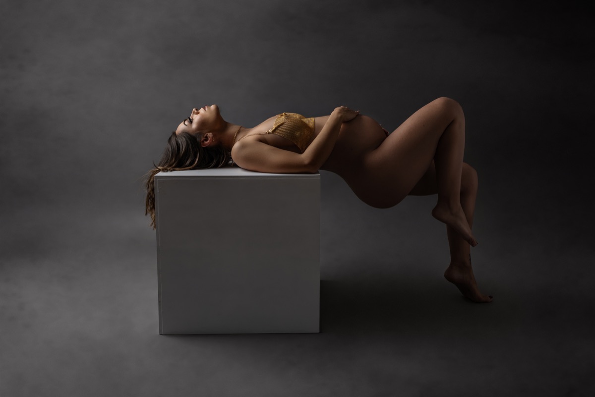 Retrato de maternidad recostada sobre un cubo en un estudio de fondo oscuro