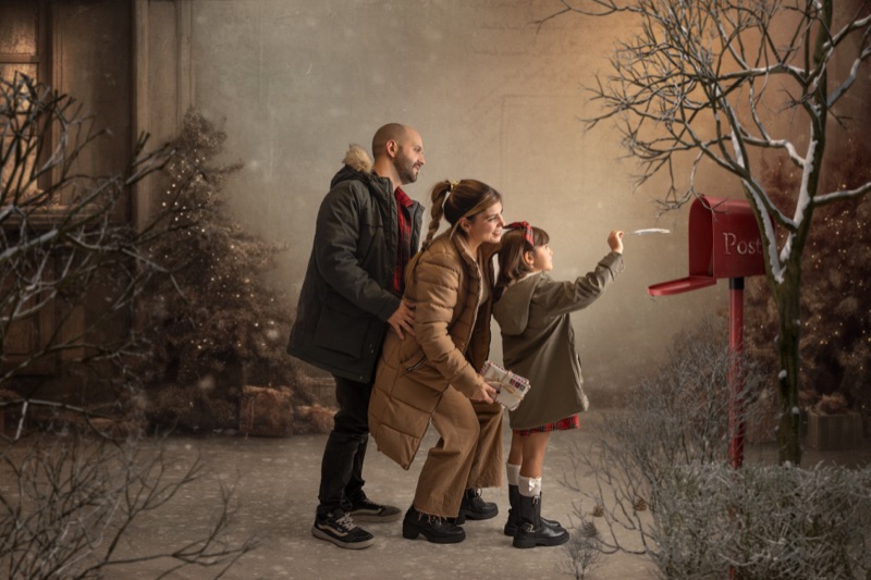 Familia preparando una carta junto a un buzón rojo de Navidad