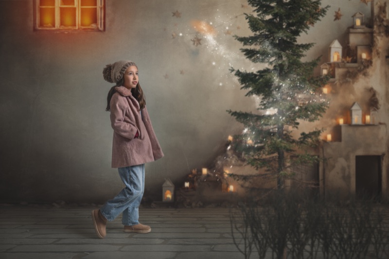 Niña junto a un árbol de Navidad iluminado en un escenario nevado