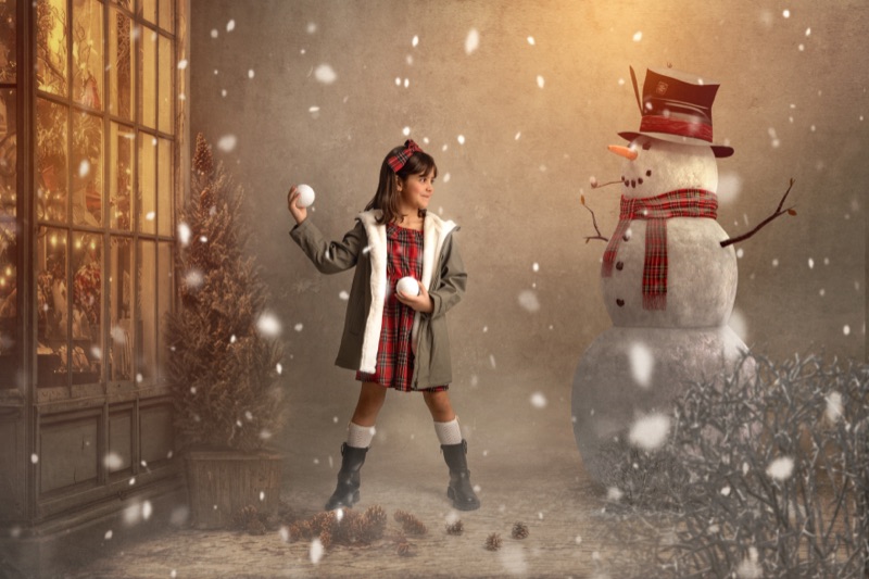 Niña jugando en la nieve junto a un muñeco de nieve