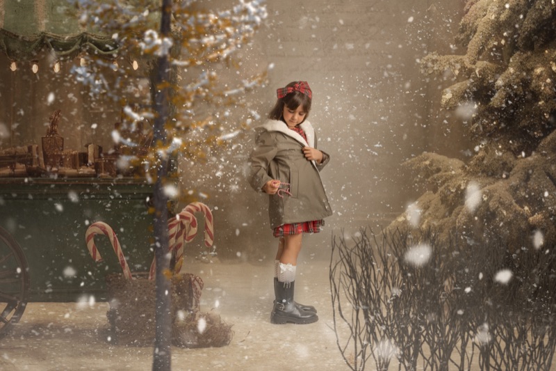 Niña con abrigo de invierno rodeada de nieve y bastones de caramelo navideños