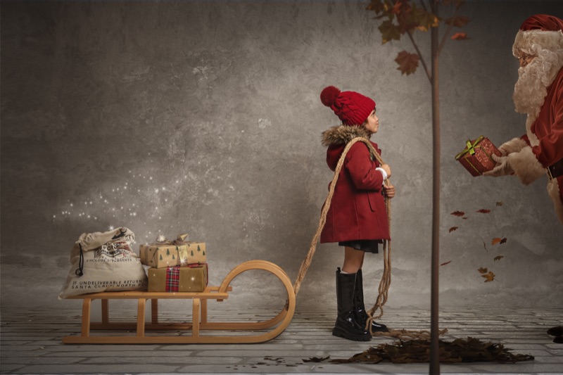 Niña frente a Papá Noel junto a un trineo y regalos