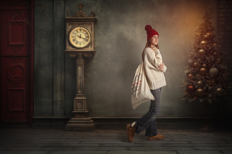 Niña con gorro rojo paseando junto a un reloj antiguo y un árbol de Navidad iluminado