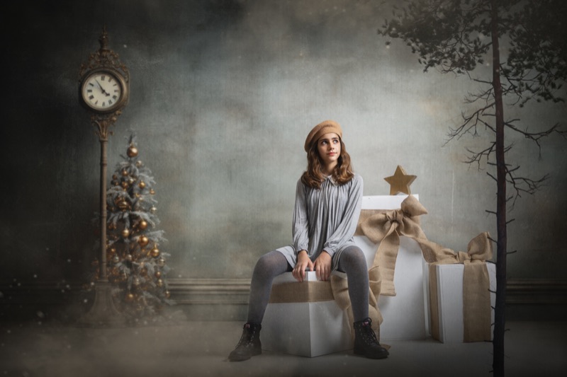 Niña sentada en un taburete entre regalos en un decorado navideño