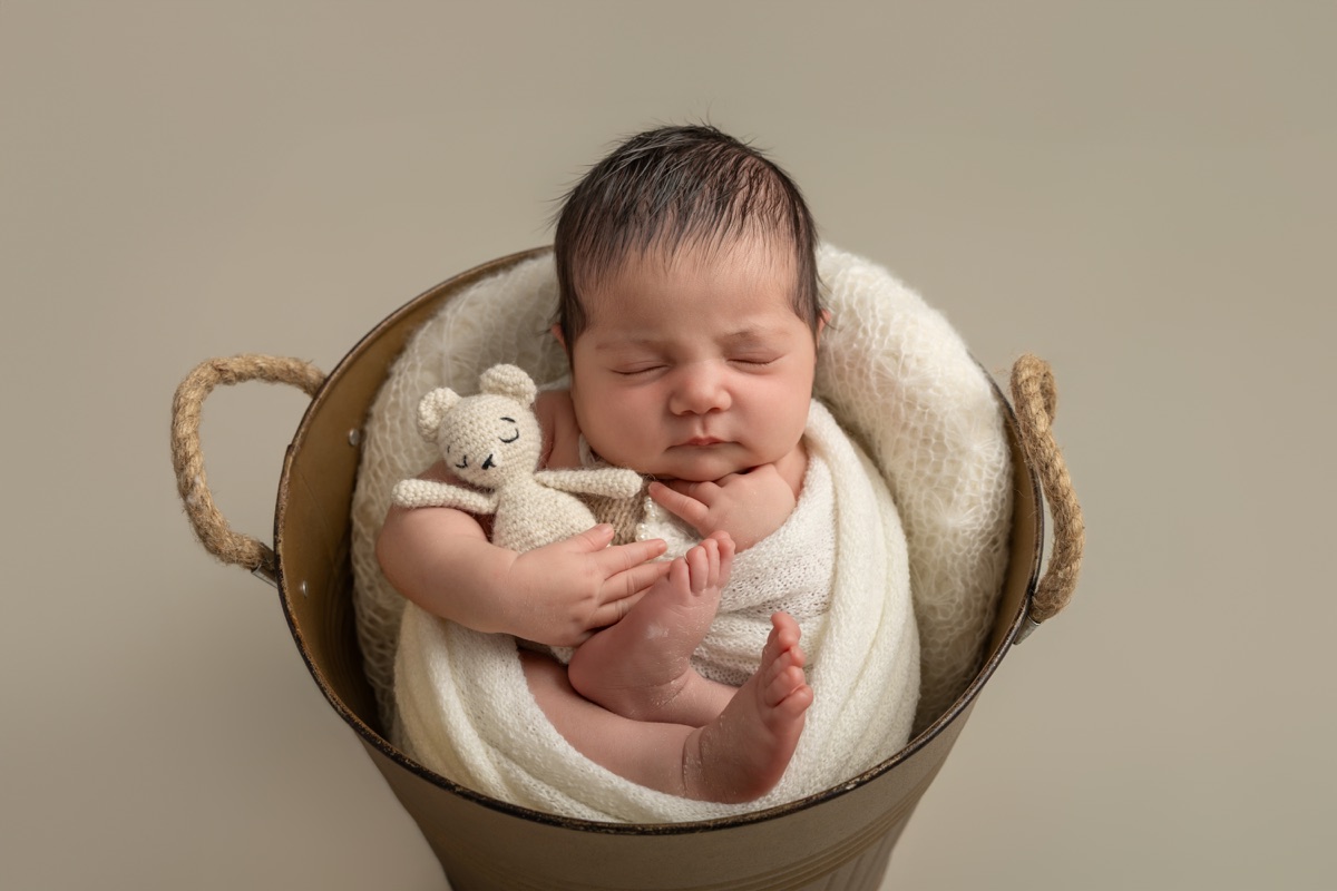 Bebé recién nacido dormido dentro de una cesta redonda, envuelto en una manta clara durante una sesión newborn en Villanueva de la Cañada