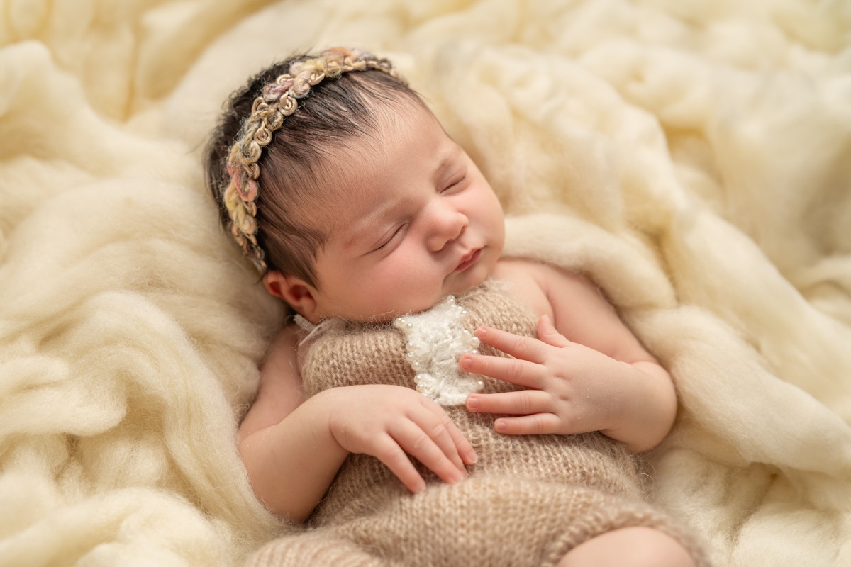 Bebé recién nacida dormida sobre una manta de punto con una delicada diadema floral durante una sesión newborn en Villanueva de la Cañada