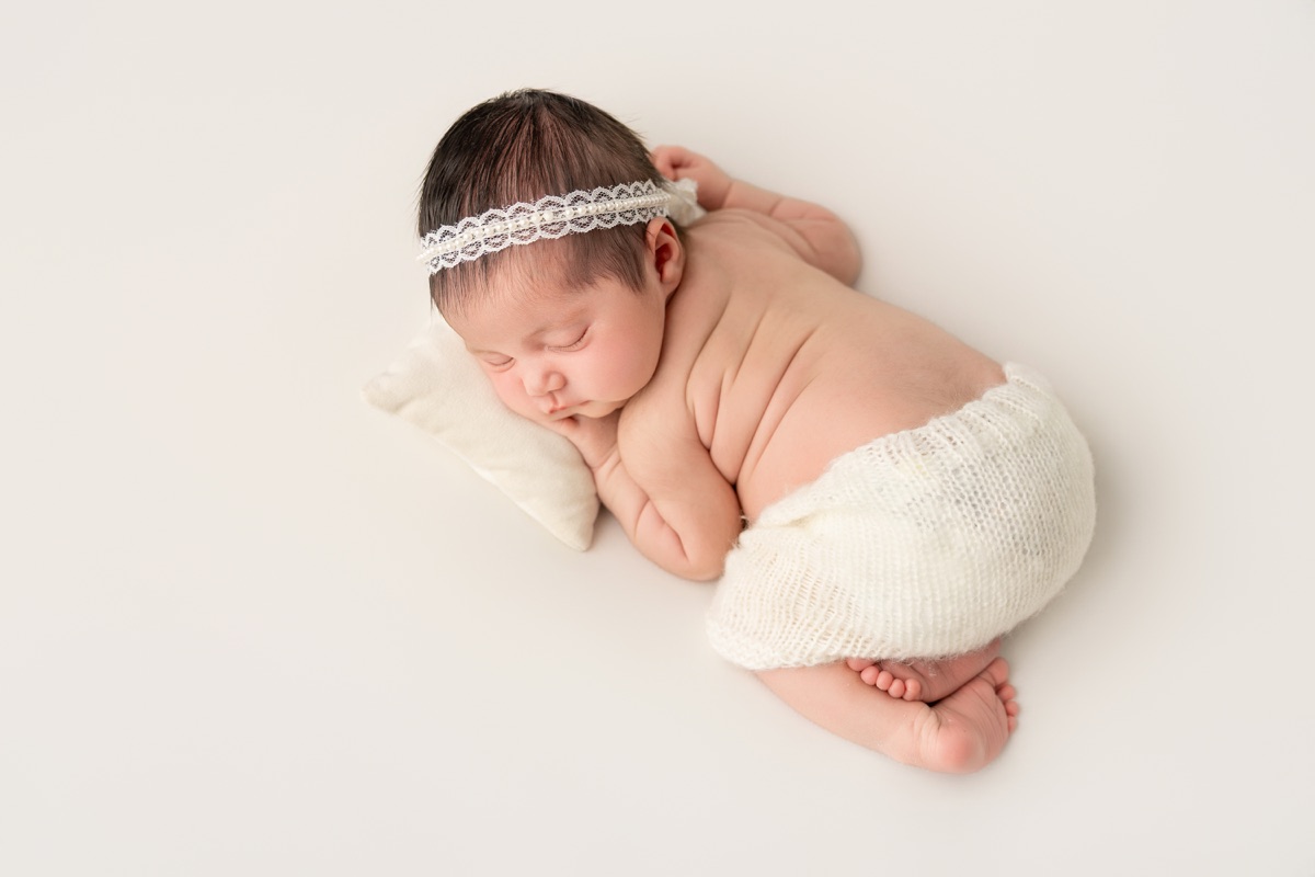 Bebé recién nacido acurrucado de lado con una diadema de encaje durante una sesión newborn en Villanueva de la Cañada