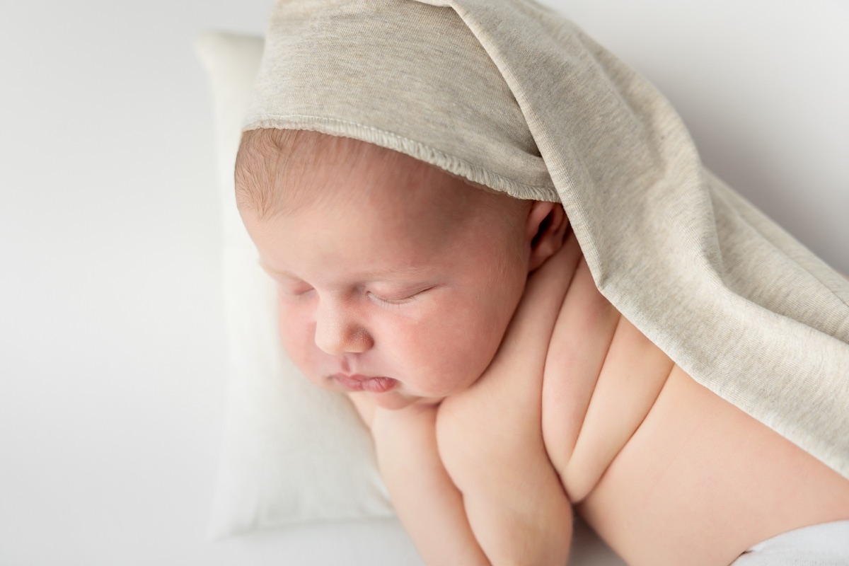 Primer plano de un bebé recién nacido dormido bajo una manta suave durante una sesión newborn en Villanueva de la Cañada
