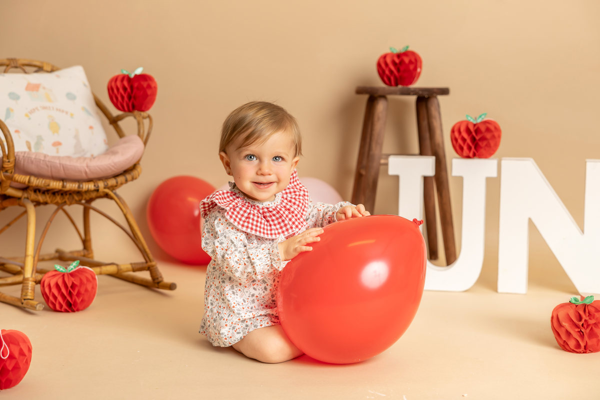 Bebé jugando con un globo rojo durante una sesión Smash Cake.