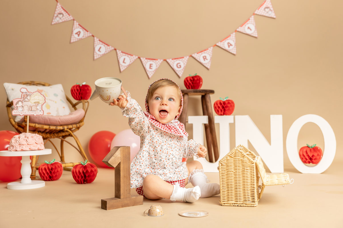 Bebé sonriente en un decorado Smash Cake con frutas decorativas y banderines.