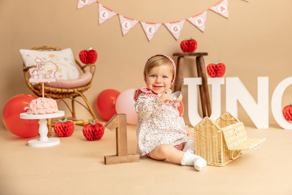 Bebé sentada junto a un decorado de cumpleaños Smash Cake en tonos rosa y beige.