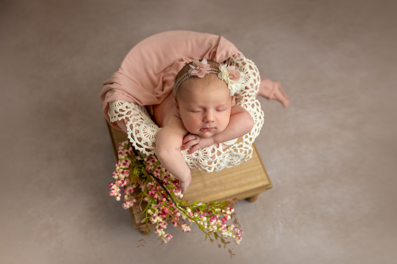 Bebé recién nacida dormida sobre un cojín rosa con flores durante una sesión newborn