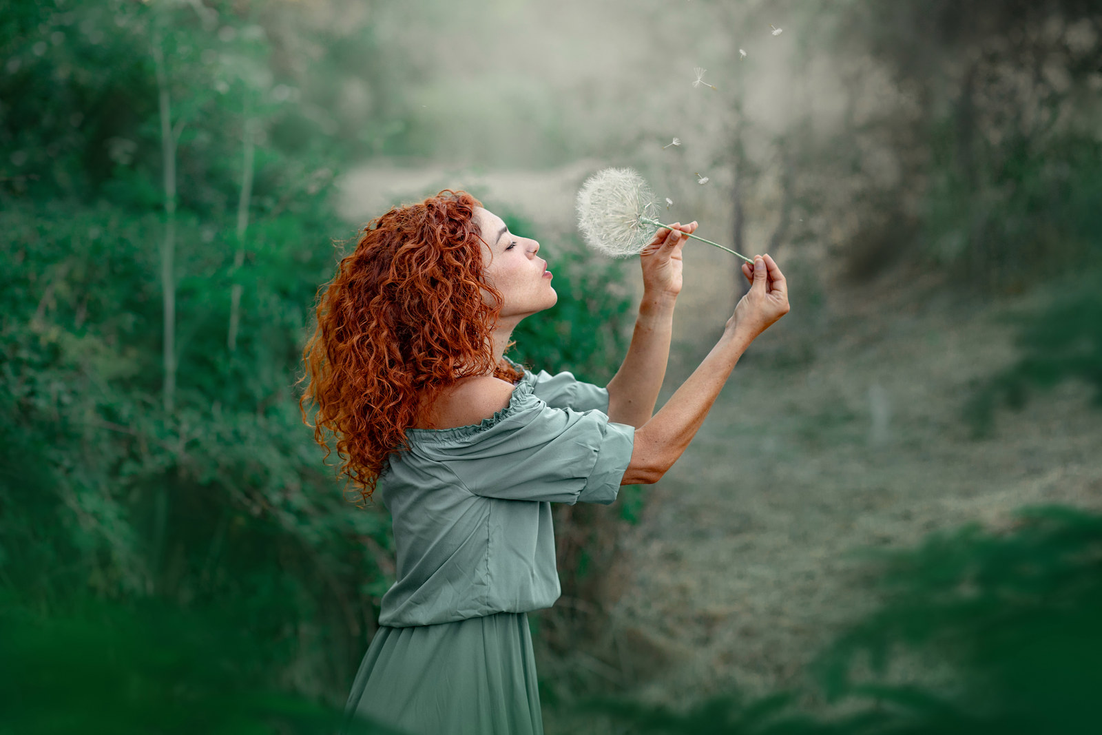 Retrato fine art en exteriores de una mujer soplando un diente de león