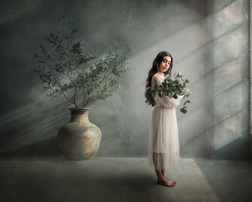 Retrato Fine Art de una mujer con vestido claro y ramas de eucalipto junto a una ventana